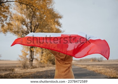 A little boy is holding the flag of Poland in nature. A child runs along the road with a flickering national flag in his hands. Concept of national holidays and patriotic events. Independence Day.