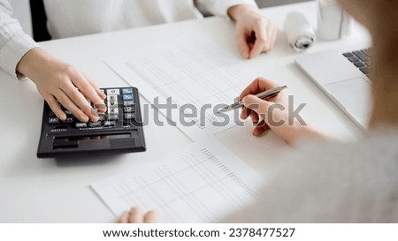 Two accountants using a laptop computer and calculator for counting taxes at white desk in office. Teamwork in business audit and finance