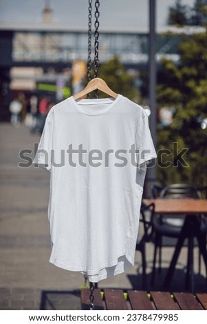 White T-shirt with short sleeves hanging on a hanger on the street. Mock-up.