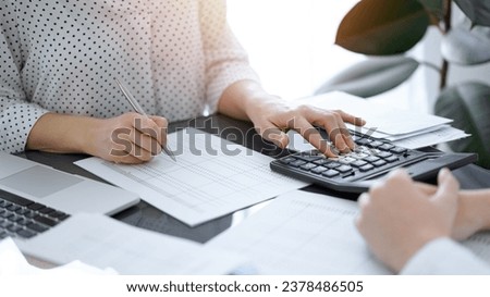 Woman accountant using a calculator and laptop computer while counting taxes with a client or a colleague. Business audit team, finance advisor