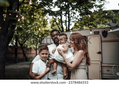 Mixed race family with white son and infant swarthy daughter spend time together in camper park outdoor. African american man with his fair skinned wife and kids enjoying summer vacation in open air Royalty-Free Stock Photo #2378486553