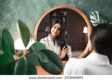 Hair care and self-care with beautiful Indian woman looking in mirror touching her healthy long hair sitting at the dressing table. Royalty-Free Stock Photo #2378486891