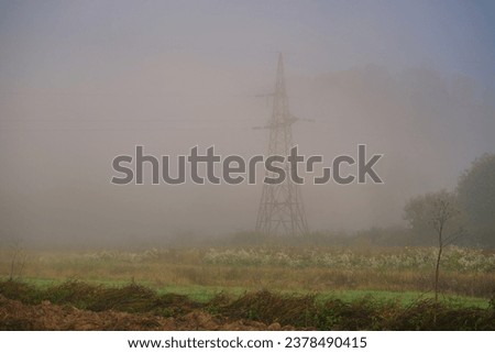 Power line support in thick fog on a field. Autumn fog hides the structure