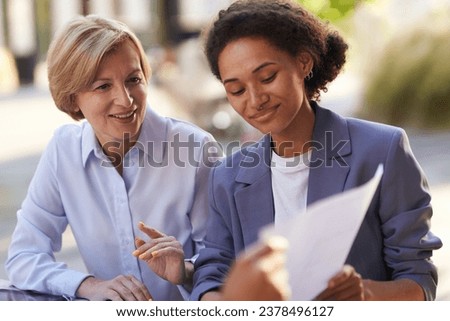 Two smiling business coleagues working with documents sitting outdoors of office
