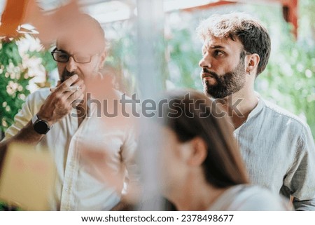 A diverse group of professionals collaborate in a modern office, sharing knowledge and ideas. They strategize and work persistently on a successful project using sticky notes on a glass wall. Royalty-Free Stock Photo #2378498677