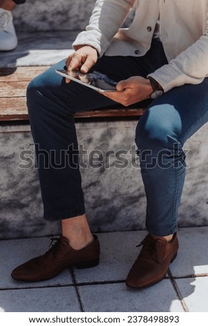 Stylish businessman sitting on a bench outdoors holding tablet. Cropped photo