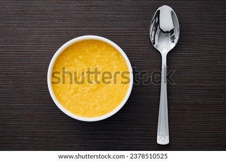 A bowl of pumpkin porridge with a silver spoon on a textured dark brown table - an appetizing blend of Thanksgiving and healthy dining, embodying the essence of nourishing traditions. Top view.