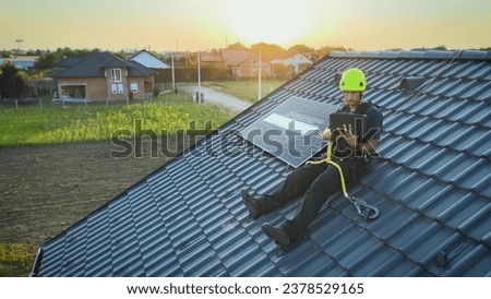 Engineer Sitting On The Roof Checking The Solar Panel Installation Using Tablet Computer With Digital Animation