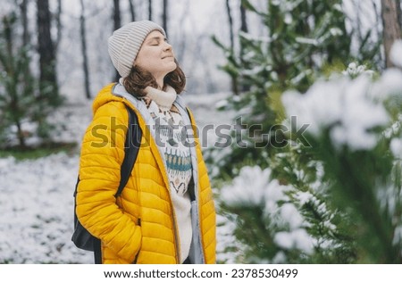 Young  adult caucasian woman in a hat and yellow jacket breathing fresh air in the winter forest