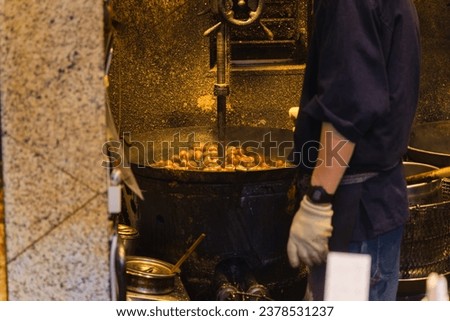 picture of a man at a street food stand roasting chestnuts in an old roasting machine