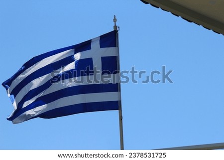 Greece flag on a background of blue sky and the wall of a building with a tiled roof