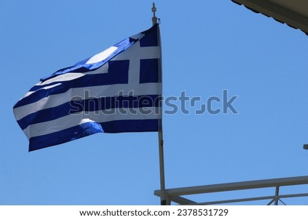 Greece flag on a background of blue sky and the wall of a building with a tiled roof