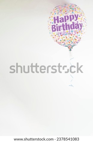 a helium balloon decorated with colored dots and a happy birthday message, with a hanging ribbon, copy space, vertical