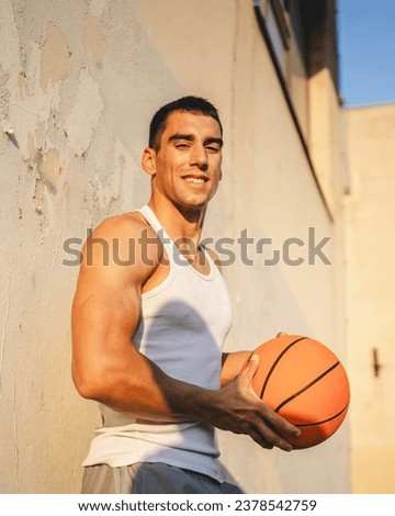 One young caucasian man male athlete stand outdoor hold basketball ball wear white tank top a-shirt strong muscular real person copy space happy smile confident healthy lifestyle concept