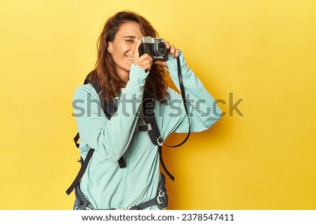 Middle aged woman mountain-ready with vintage camera on yellow