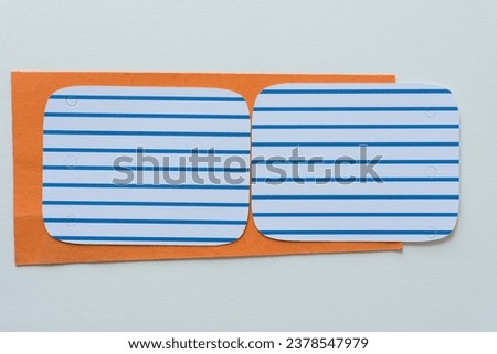 two machine-cut blue and white striped paper rectangles with rounded corners on orange and blank paper background