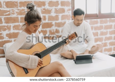 Asian woman play guitar while man do freelance work from home.