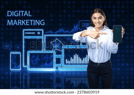 Attractive happy european businesswoman pointing at smartphone on blue pixel background with gadgets and business chart hologram. Digital marketing, finance, social network and online service concept