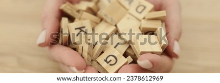 Hands of woman with neat manicure holding wooden cubes with English letters. Female person sits at table showing handful of children toy blocks