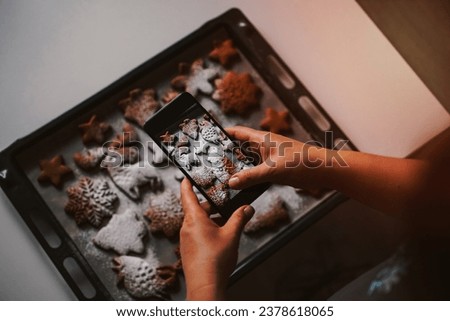 A woman takes a photo on a smartphone Christmas gingerbread sprinkled with powdered sugar. Headless shot, selective focus , winter holidays spirit