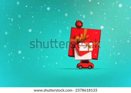 Minimal Christmas card concept, red small car transports a many Christmas gifts under snowfall, blue background. 