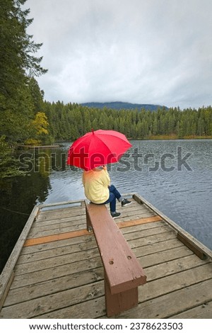 A woman sits on the edge of a bench on a dock holding a red umbrella at Robinson Lake in north Idaho.