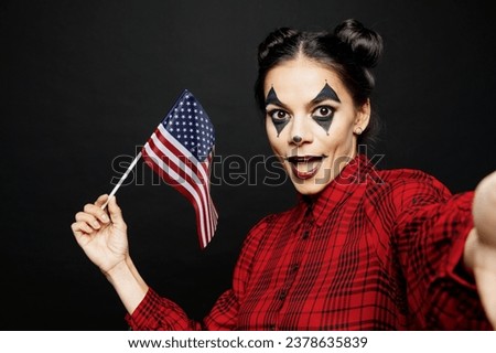 Young woman with Halloween makeup face art mask wears clown costume red dress do selfie shot mobile cell phone hold American flag isolated on plain black background studio. Scary holiday party concept