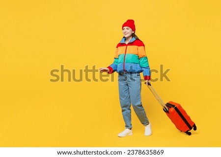 Traveler woman wear padded windbreaker jacket red hat hold suitcase bag go isolated on plain yellow background. Tourist travel abroad in free spare time rest getaway. Air flight trip journey concept Royalty-Free Stock Photo #2378635869