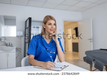 Portrait of young female doctor sitting in clinic office, filling out medical form at table.