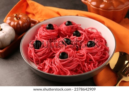 Red pasta with olives in bowl on grey textured table, closeup. Halloween food
