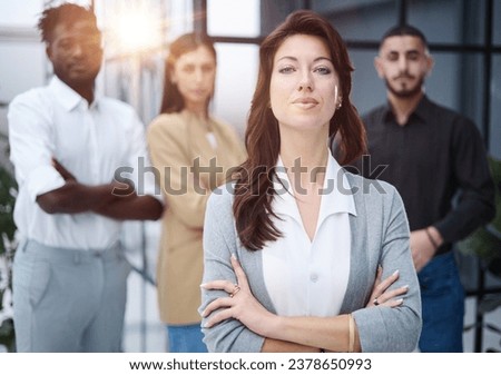 Portrait of a young woman standing in an office with colleagues in the background.