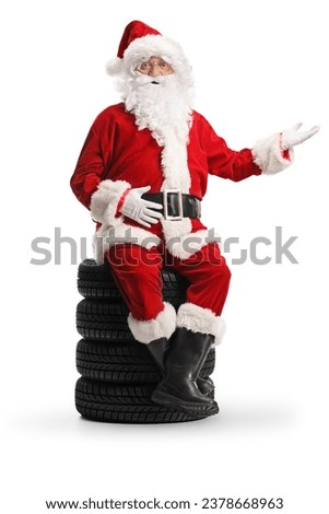 Santa claus sitting on a pile of tires and showing with hand isolated on white background
