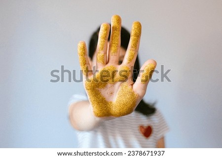 Unrecognizable young girl showing her palm hand covered of golden glitter while doing stop sign. Concept of European Union ban use of microplastics. Selective focus on hand.