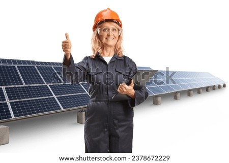 Female worker in a uniform wearing helmet and goggles and gesturing thumbs up at a solar farm isolated on white background