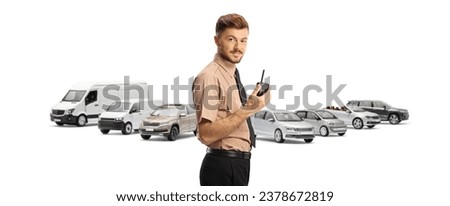 Young security guard holding a walkie talkie in front of parked vehicles isolated on white background
