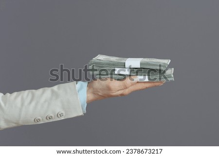 Closeup on female worker in a light business suit with dollars money packs isolated on gray.