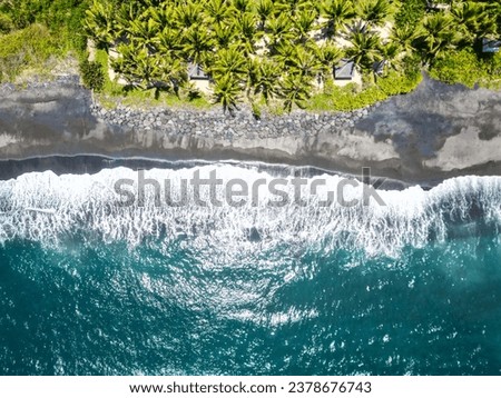 Top aerial drone view of the beach, black sand, palm tropical island paradise, turquoise water, ocean waves in Bali