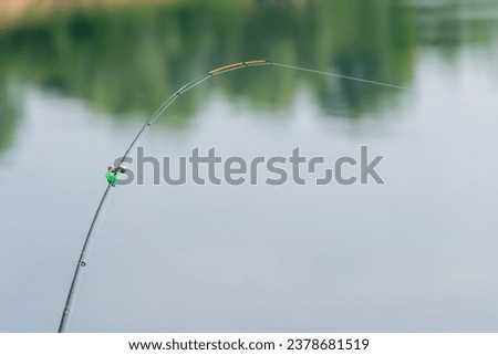 Part of a fishing rod with a stretched fishing line against the background of water. Background for the theme of recreation on fishing. Royalty-Free Stock Photo #2378681519