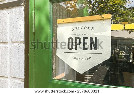 Text on vintage white sign " welcome we' are Open come on in " in a coffee shop.
