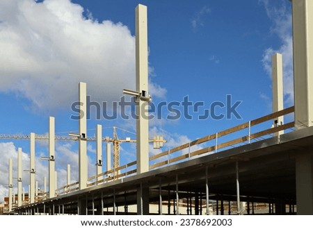 Metallic pillars of large building under construction with scaffolding and a tower crane on background.