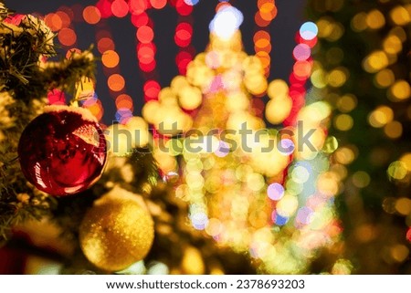 The lights of the garland decorate the house and the Christmas tree, on the branch there is a red sparkling ball. Christmas tree in the evening city on New Year's Eve. Christmas mood.