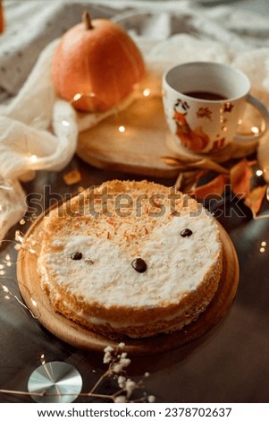 A cake in the form of an animal fox stands on a wooden board on the table against the background of a wrapped pumpkin and a mug of tea
