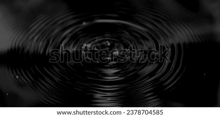 Ripple of water or water drop splash on black background. Abstract shape out of the water. Oil ripples from a drop of water in the dark. Rippled liquid with mood effect in black and white.