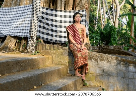 Balinese girl in festive clothing and headdresses sit on the steps of a temple