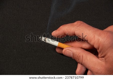 Hand of a European adult man holding a lit cigarette with his fingers Royalty-Free Stock Photo #2378710799
