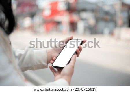 Close-up image of a woman using her smartphone while walking down the street in the city. A white-screen smartphone mockup. chatting, using map on her phone, searching something on the internet