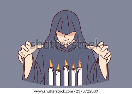 Man monk in hood stands over burning candles, performing mysterious religious ritual to communicate with otherworldly world. Monk experiments with black magic and practices witchcraft Royalty-Free Stock Photo #2378722889
