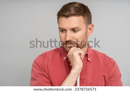 Sad pensive thoughtful man touching chin looking down isolated on gray background. Bearded serious middle aged caucasian blond guy wistfully thinking. Placard, poster. Sincere human emotions concept. Royalty-Free Stock Photo #2378726571