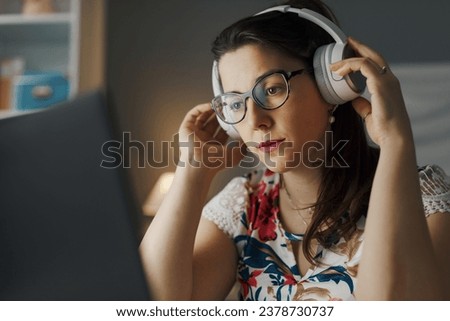 Young woman wearing headphones and watching videos on her laptop at night