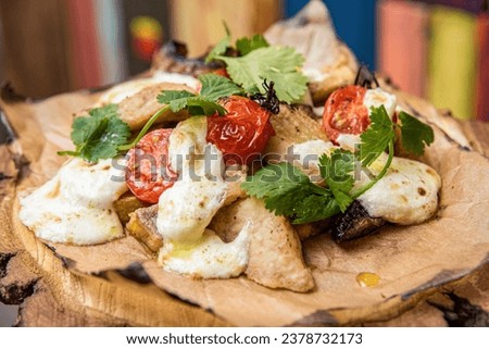 Slices of white fish with grilled vegetables baked with cheese cream sauce. Decorated with cilantro leaves. On a wooden plate and a colored background Royalty-Free Stock Photo #2378732173